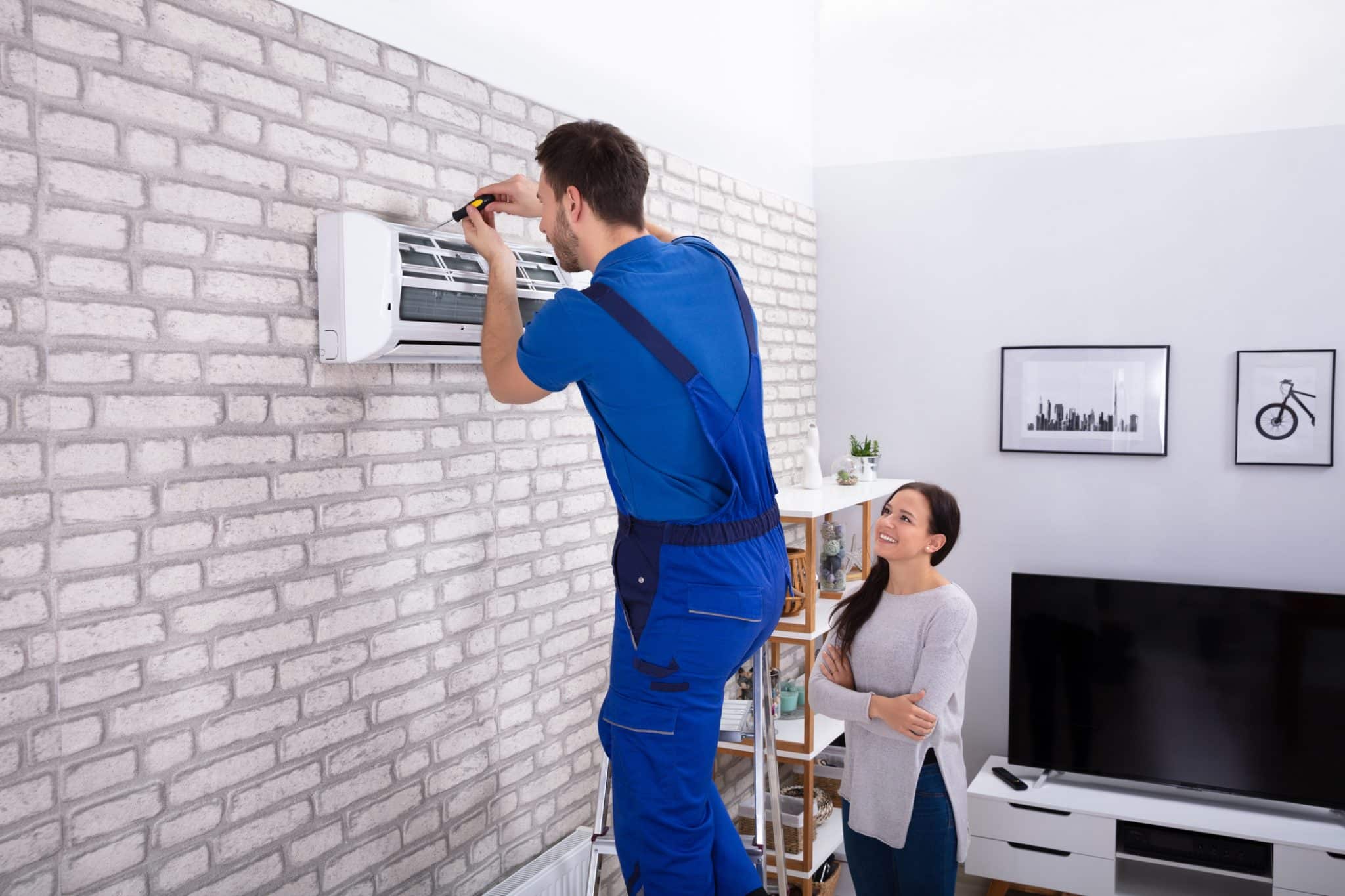 A woman smiles as an AC technician installs her new ductless HVAC unit, making temperature control easier.