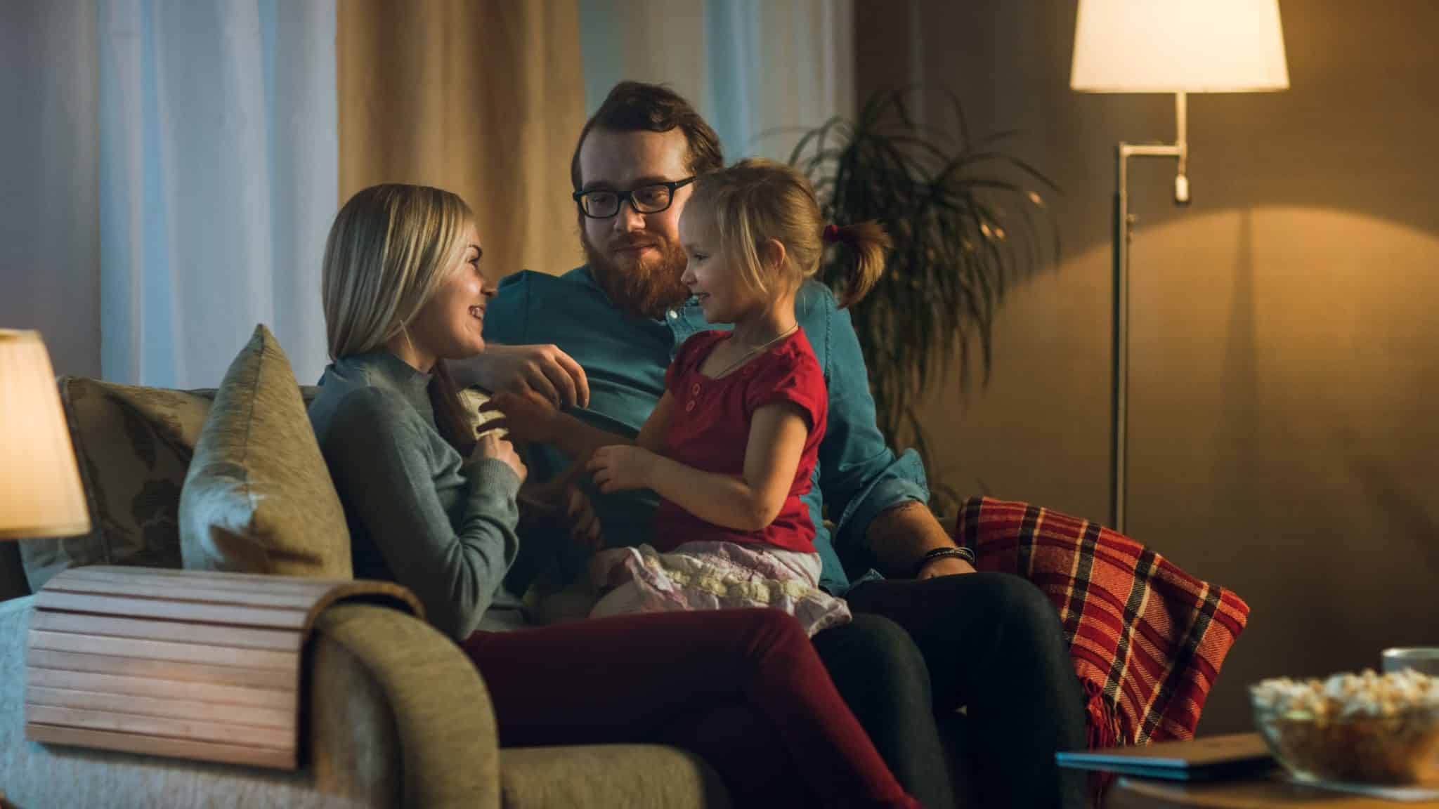 A couple who has evaluated the best HVAC systems for their home sits on the couch with their little girl, looking cozy and comfortable.