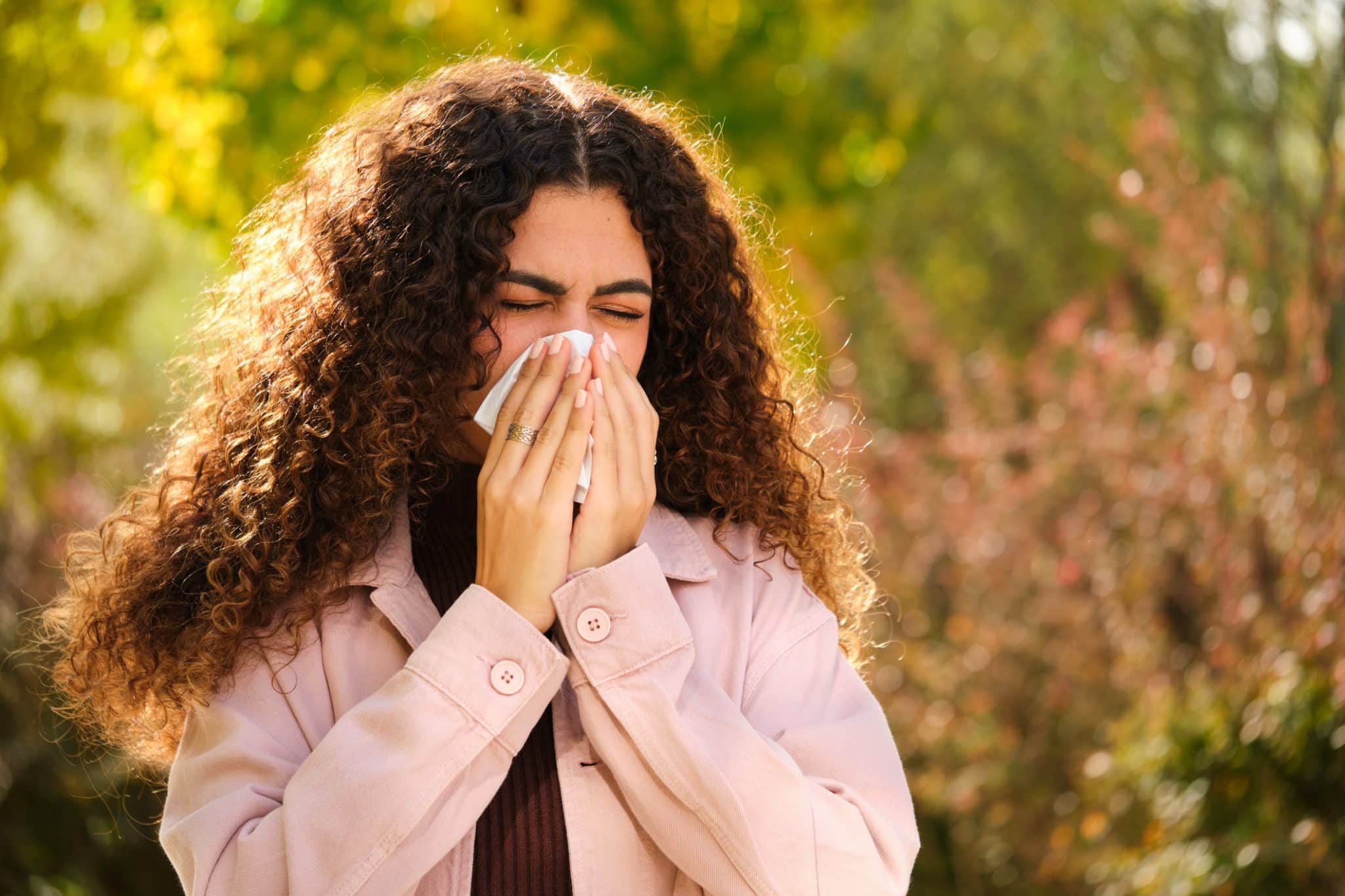 A young woman blows her nose, reacting to hay fever. She could benefit from whole home air purification.