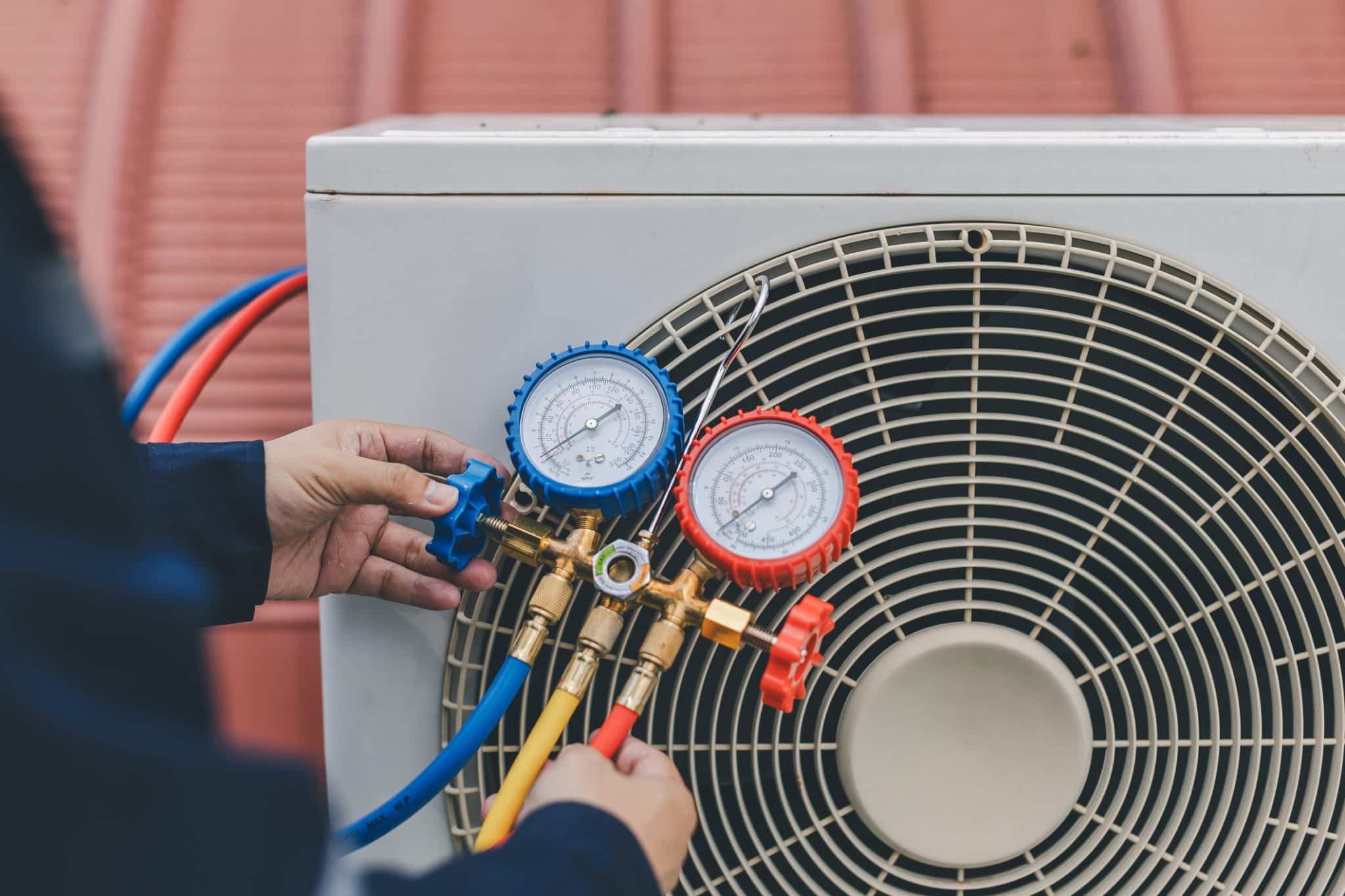 A photo of a technician holding gauges in front of an AC unit they’re checking.