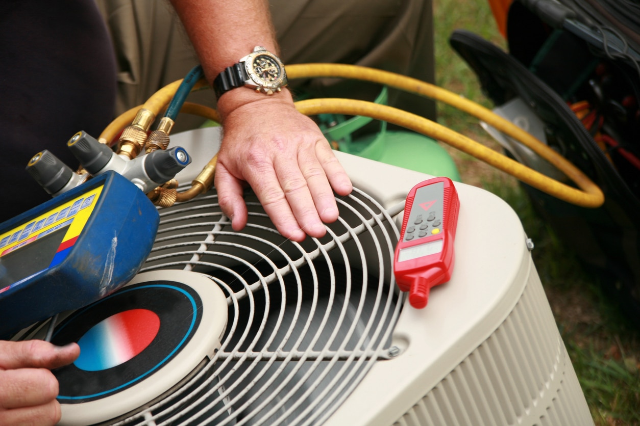 Technician servicing an air conditioning unit with tools and gauges for maintenance and repair.