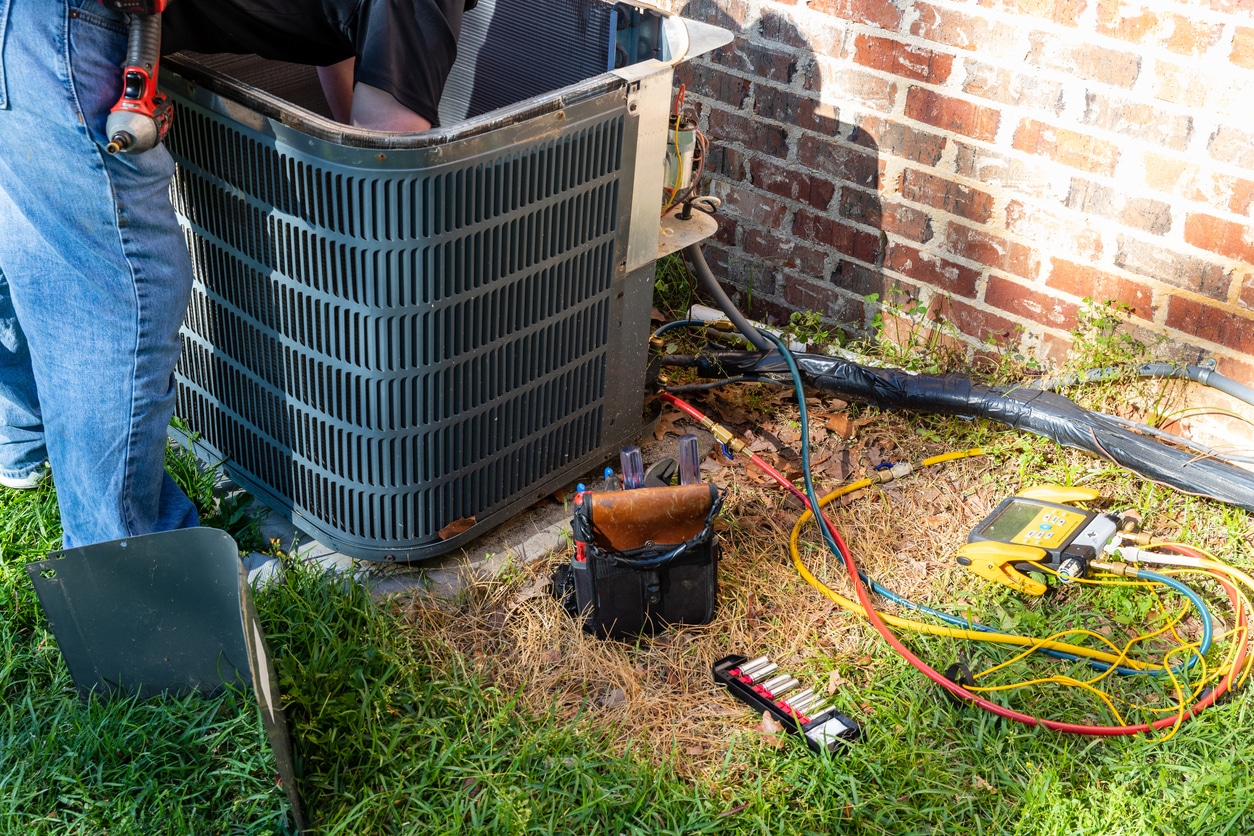 Outdoor AC unit being serviced by HVAC technician in spring for pre-summer AC maintenance