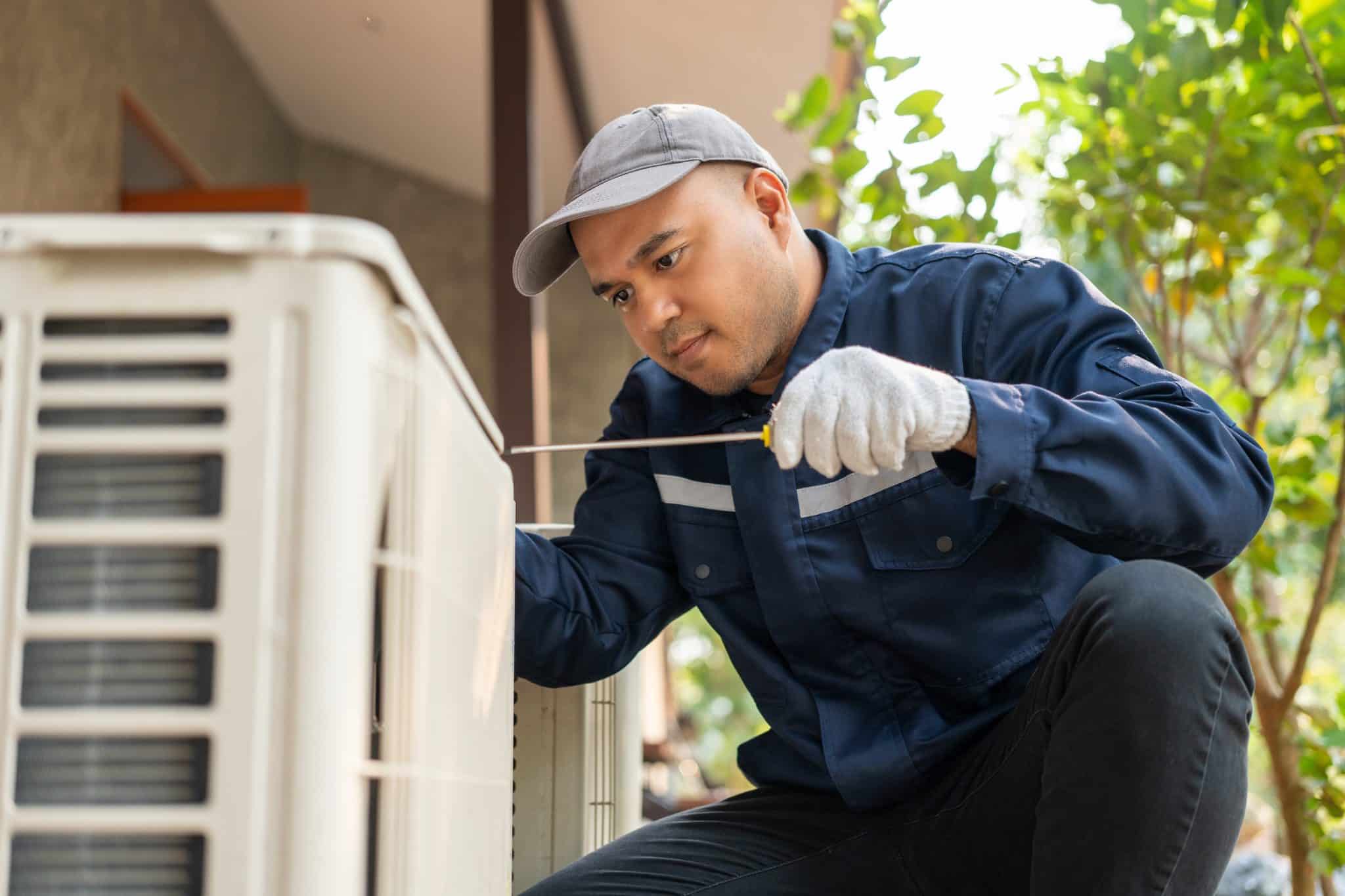 Technician repairing outdoor air conditioning unit with screwdriver.